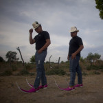 Two young Mexican men wearing cowboy hats and pink cowboy boots with 24 inch toes curving upwards.