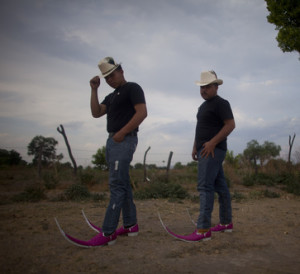 Two young Mexican men wearing cowboy hats and pink cowboy boots with 24 inch toes curving upwards.